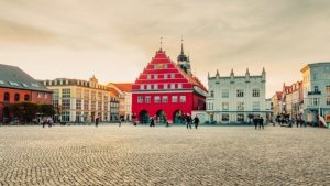 Marktplatz_Greifswald2019(WallyPruss)_2_ganzes_Bild_2_Youtube © Wally Pruß Der Greifswalder Marktplatz. Neben dem roten Rathaus ist eine Apotheke. Vor dem Rathaus steht ein Tasmodell