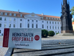 Gutscheinbuch Heimathafen Greifswald 2022 © Theres Behnke Foto des Gutscheinbuches Heimathafen Greifswald 2022 vor dem Universitätshauptgebäude