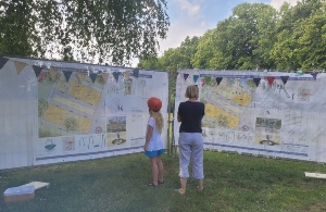 Bürgerbeteiligung zum Spielplatz im Rosengarten © Stadtverwaltung der Universitäts- und Hansestadt Greifswald Ein Mädchen und ihre Mutter schauen sich die zwei Spielplatzvarianten auf großen Bannern an