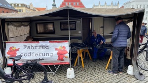 Fahrradcodierung April 2023, Foto Pressestelle © Pressestelle Ein Mitarbeiter der ABS unterhält sich mit einem Bürger in seinem Zelt, vor sich das Fahrrad eingespannt, um es zu codieren