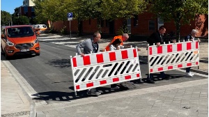 Pressestelle Füf Personen tragen auf einer Straße zwei Verkehrsbaken zur Seite