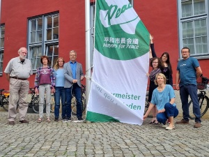 Hissen der Mayors for Peace Flagge © Pressestelle der Universitäts- und Hansestadt Greifswald Mitglieder der Bürgerschaft, der Oberbürgermeister und Mitarbeitende des Beauftragtenbüros hissen der Mayors for Peace Flagge vor dem Rathaus
