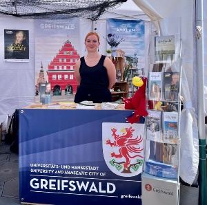 Internationale Hansetage 2023 © Gudrun Koch, Greifswald Marketing GmbH Eine Mitarbeiterin der Greifswald Marketing GmbH steht am Infostand der Universitäts- und Hansestadt Greifswald bei den 43. Internationalen Hansetagen in der polnischen Hansestadt Toruń