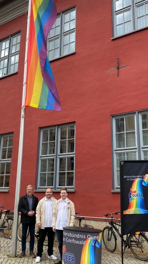 OB Dr. Fassbinder, Thomas Jager und Lukas Kretschmer von queer hissen die Regenbogenfahne am Rathaus, Foto Pressestelle © Pressestelle OB Dr. Fassbinder, Thomas Jager und Lukas Kretschmer von queer vor der Regenbogenfahne am Rathaus