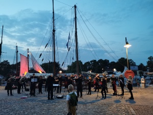 Blasorchester Greifswald am Museumshafen © Theres Behnke, Greifswald Marketing GmbH Musiker des Blasorchester Greifswald stehen am Museumshafen vor einem Traditionsschiff und spielen ein Konzert